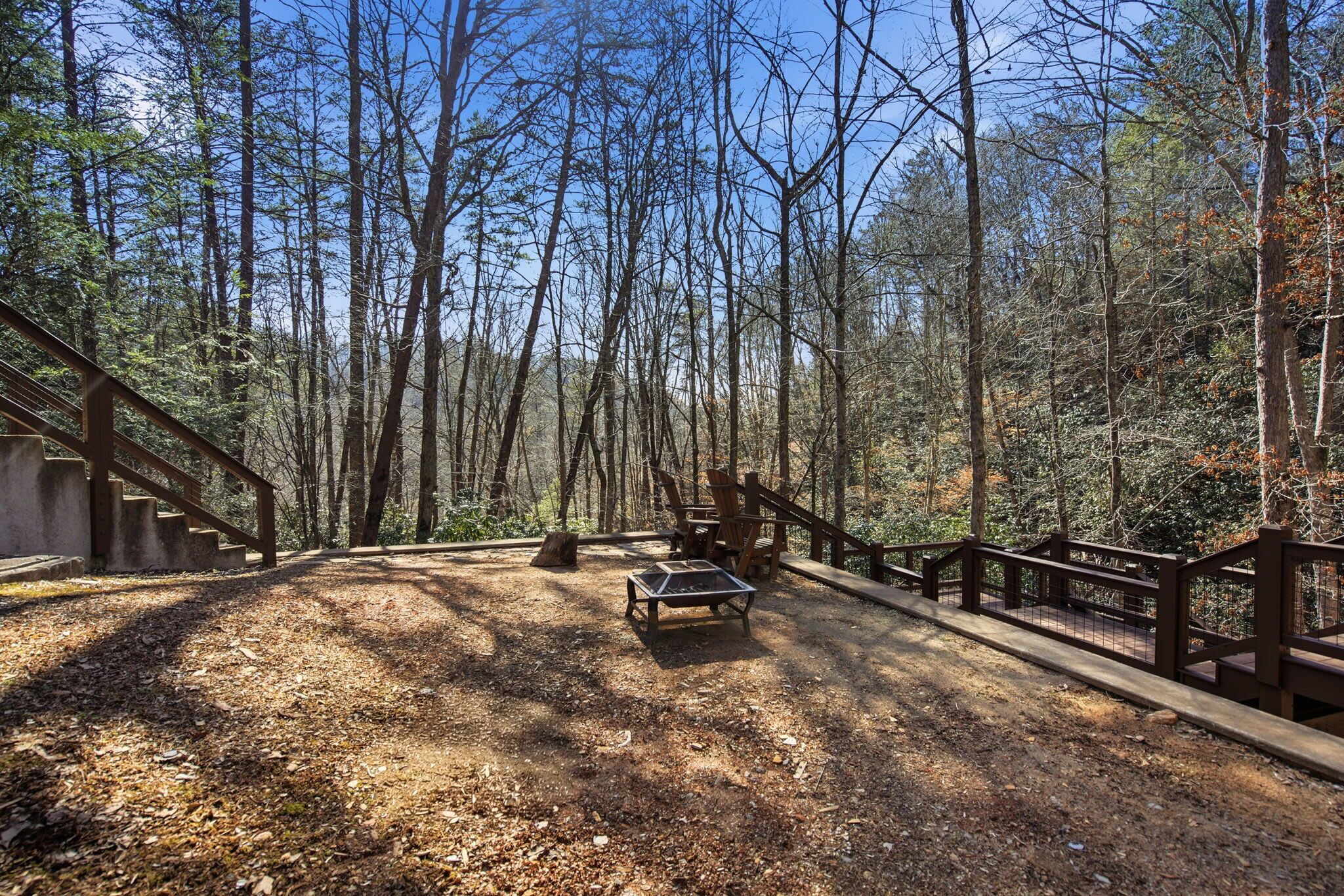 A forested area with a wooden deck, a picnic table, and a bench.