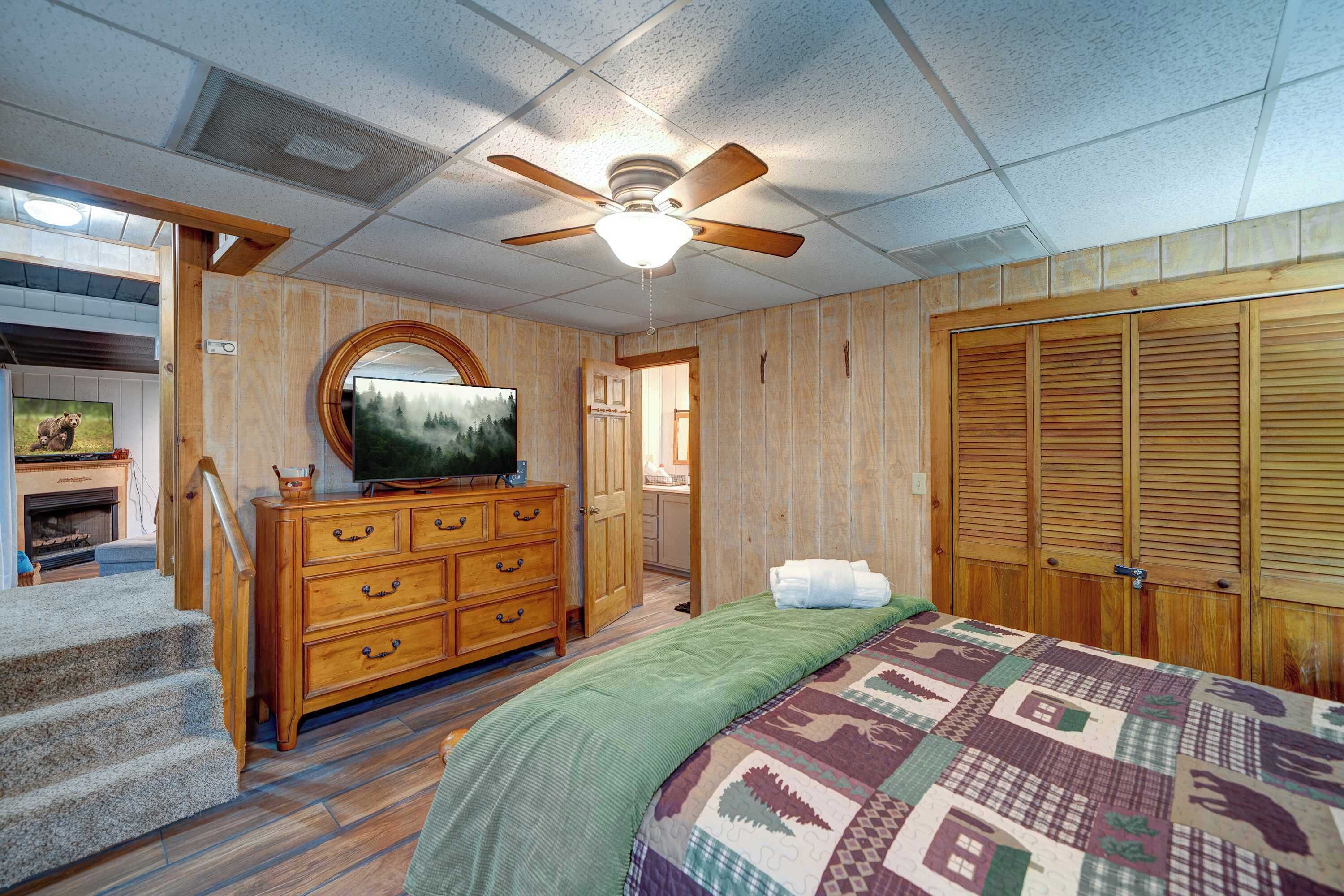 A bedroom with a wooden floor, a bed with a quilt, a dresser, a television, and a ceiling fan.
