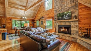 Interior acogedor de una cabaña con chimenea de piedra, paredes de madera y un ventanal con vistas a la vegetación.
