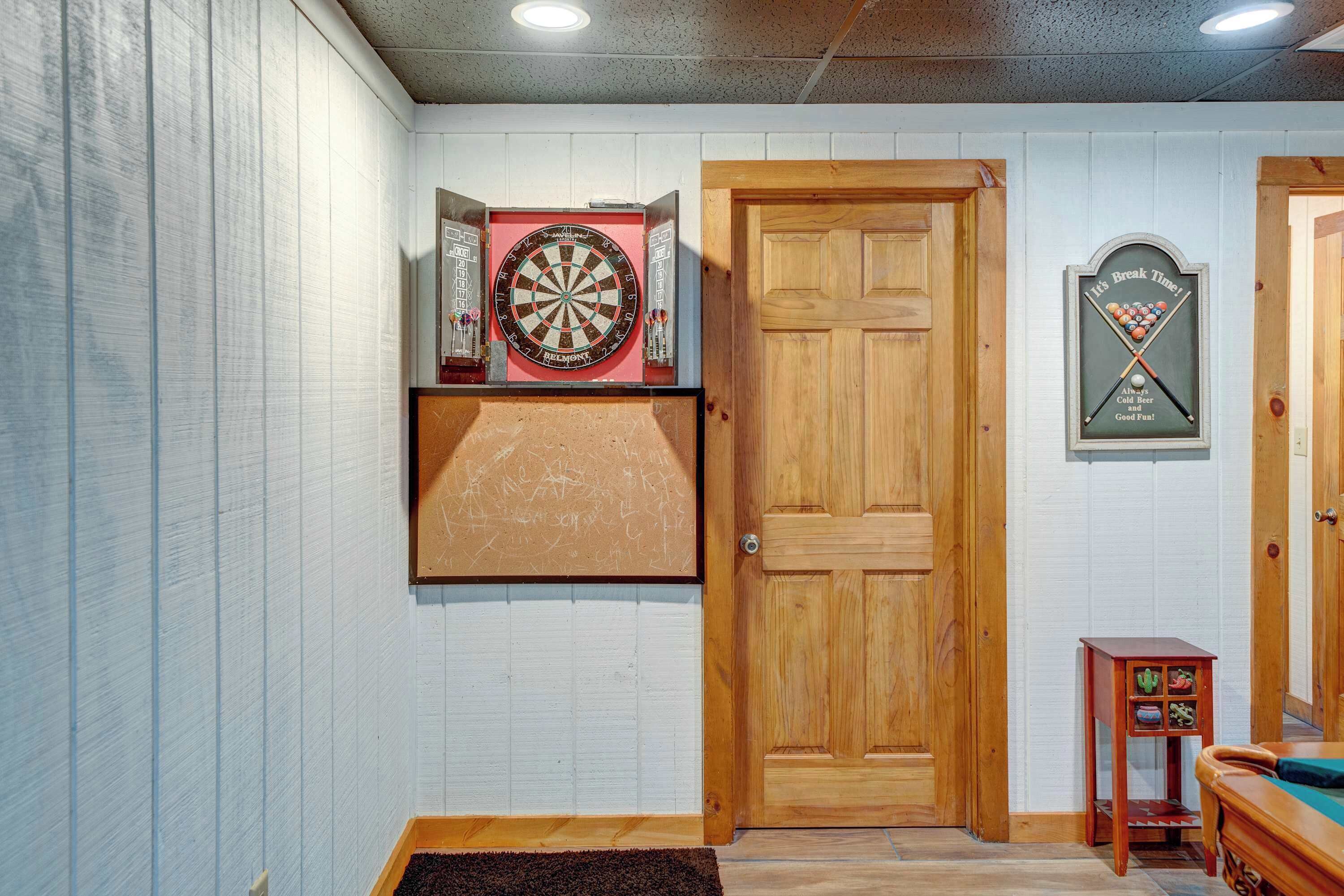 A room with a wooden door, a dartboard, a framed dartboard, and a small table with a plant.