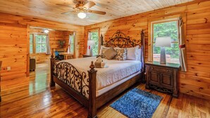 Un dormitorio de cabaña de madera con una cama, un ventilador de techo y vistas al exterior a través de una ventana.