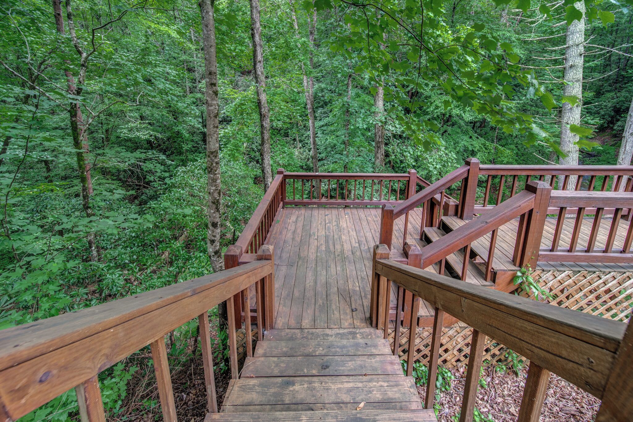 A wooden staircase leading into a forested area with railings on both sides.