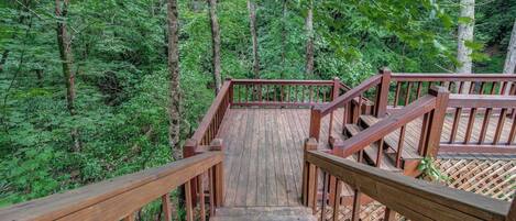 A wooden staircase leading into a forested area with railings on both sides.