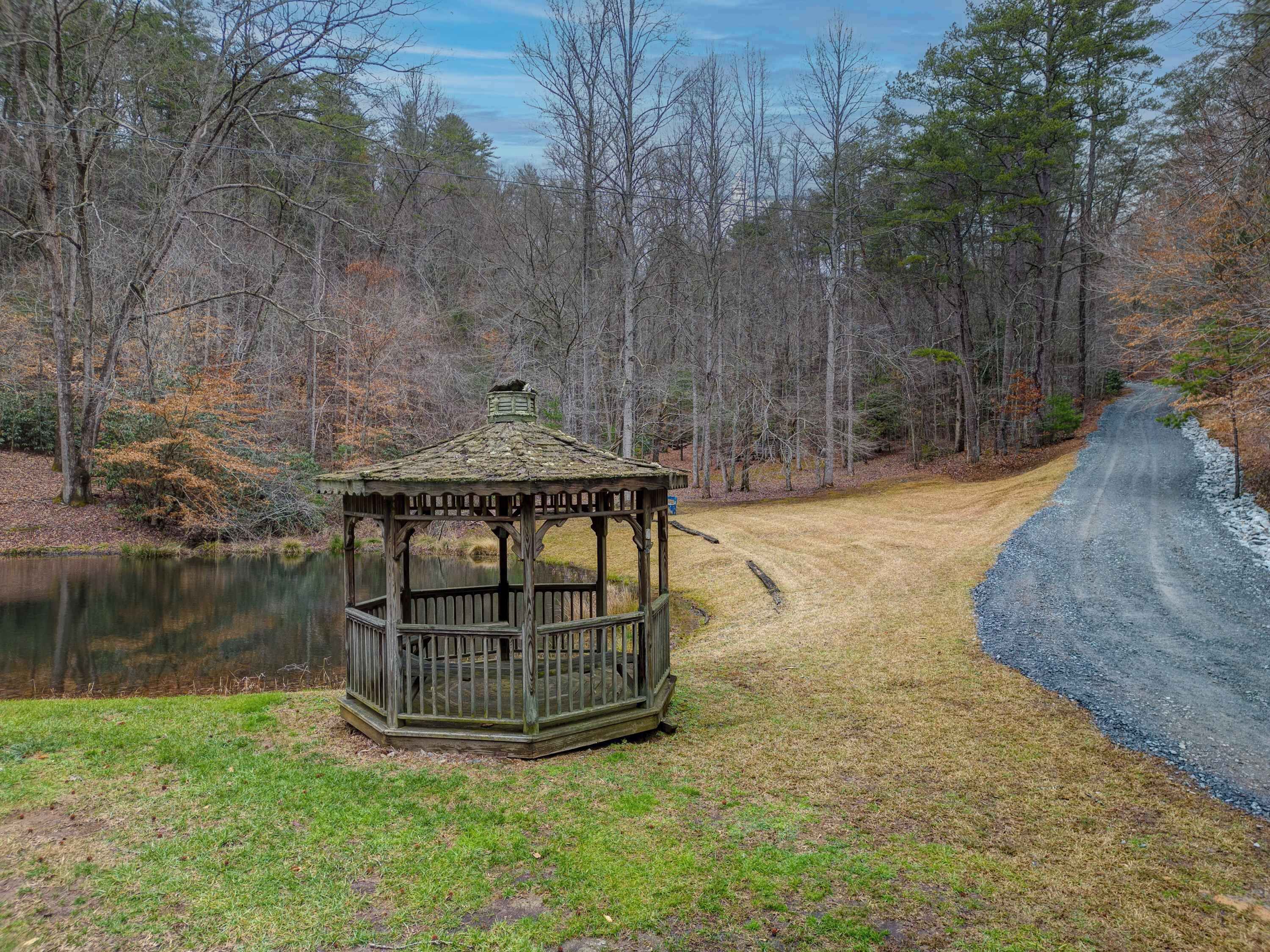 A gazebo in a wooded area with a dirt path and a body of water.