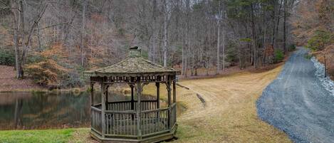 A gazebo in a wooded area with a dirt path and a body of water.