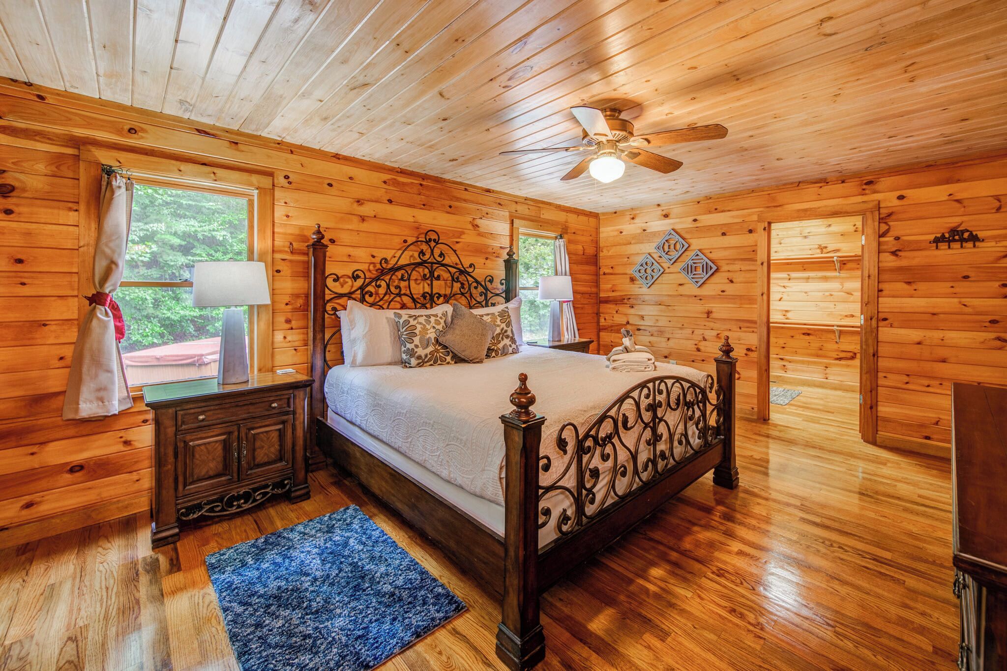 Ein Schlafzimmer einer Holzhütte mit einem Bett, Nachttischen, einem Deckenventilator und einem Fenster mit Vorhängen.