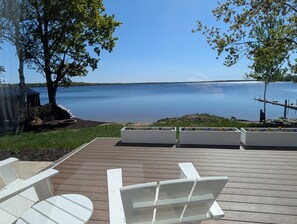 A wooden deck with white Adirondack chairs and planters with flowers, overlooking a calm lake.