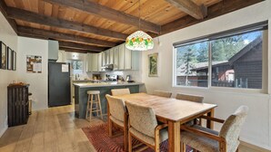 A spacious kitchen with wooden beams, a large island, and a dining area with a table and chairs. - Christmas Valley Chalet Tahoe Adventure Awaits! (South Lake Tahoe)