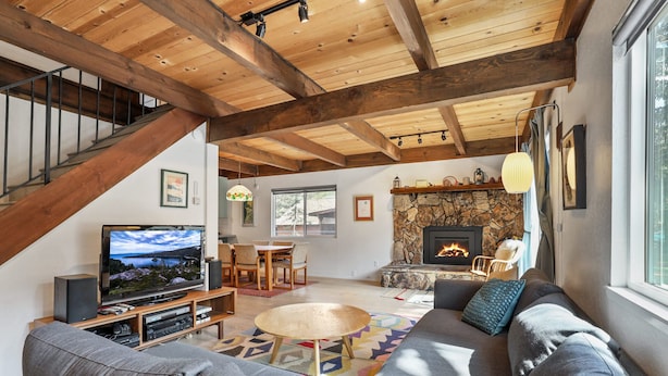 A spacious living room with a stone fireplace, a large sofa, a television, and a dining area. - Christmas Valley Chalet Tahoe Adventure Awaits! (South Lake Tahoe)