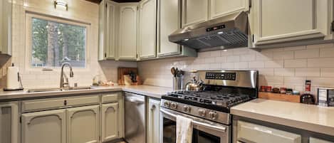 Una cocina moderna con armarios grises claros, una estufa de acero inoxidable y un ventanal que proporciona luz natural.