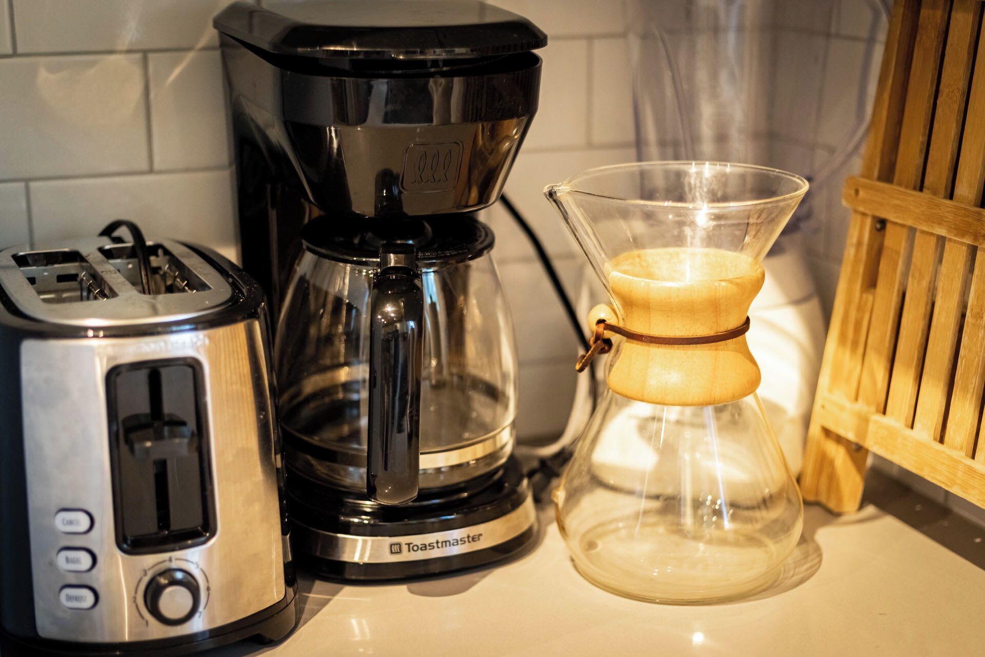 Un grille-pain, une machine à café et une carafe en verre sur un plan de travail de cuisine.
