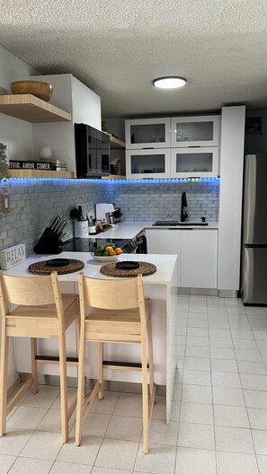 Eine moderne Küche mit weißen Schränken, einer zentralen Kochinsel mit Stühlen, einem eingebauten Backofen und einem Kühlschrank.