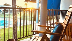 A wooden lounge chair with a cushion, a small table with a potted plant, and a railing overlooking a pool area. - Tropical Beachfront Villa (Río Grande)