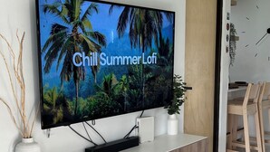A living room with a flat-screen TV mounted on a wall, a wooden cabinet below, a small white vase, and a round wooden table with a magazine. - Tropical Beachfront Villa (Río Grande)