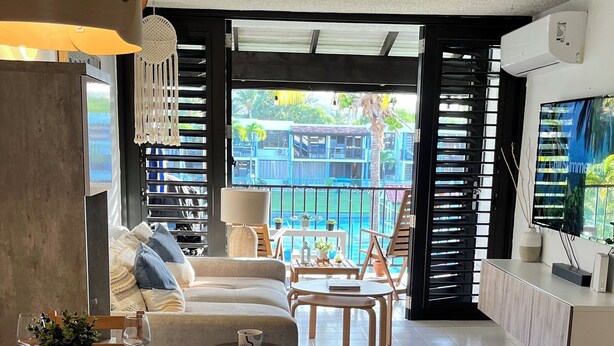 A spacious living area with a dining table set for two, a sofa, and a TV mounted on the wall. - Tropical Beachfront Villa (Río Grande)