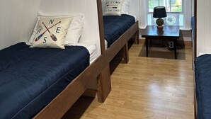 Asuntolan huone, jossa on kaksi kerrossänkyä, puinen pöytä lampun kanssa ja ikkuna, josta avautuu näkymä vehreään maisemaan.