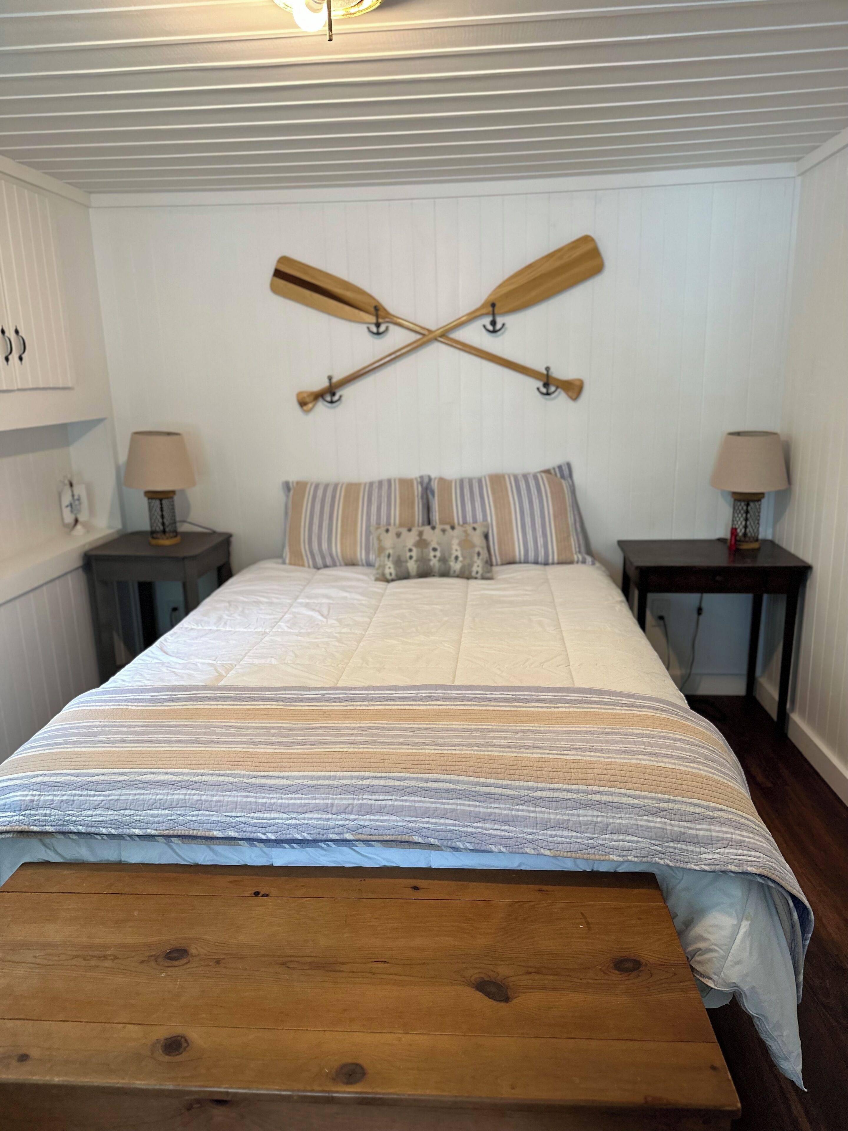 A bedroom with a bed, two nightstands, a wooden bench, and two lamps.