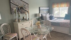 A bedroom with a bed, a bedside table, a lamp, a dresser, and a glass table with chairs.