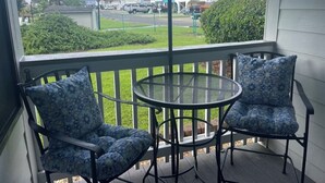 A porch with two patterned chairs and a round table, overlooking a street with buildings and greenery.