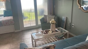 A living room with a sofa, a coffee table, and a chair. There is a sliding glass door leading to a balcony.