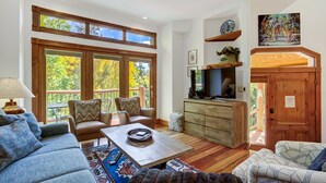 A spacious living room with a large window, a wooden cabinet, and a television. - Dogwood Retreat | 4BR Oasis with Hot Tub & Short walk to Main ST (Breckenridge)