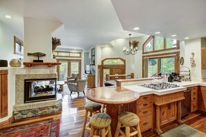 A spacious kitchen with a central island, wooden cabinets, and a fireplace. - Dogwood Retreat | 4BR Oasis with Hot Tub & Short walk to Main ST (Breckenridge)