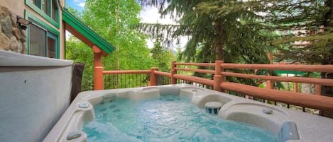 Relax in a serene hot tub on an outdoor deck surrounded by lush greenery and a stone wall.