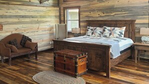 A rustic wooden room with a bed, a wooden chest, a sofa, and a ceiling fan. - Stay in the villa where the story's etched in stone  (Benton)