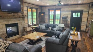 A cozy living room with a fireplace, leather sofas, wooden flooring, and a flat-screen TV mounted on the wall. - Stay in the villa where the story's etched in stone  (Benton)