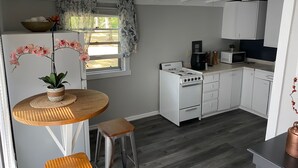 Ett modernt kök med vita skåp, en gasspis, en mikrovågsugn och en matplats med ett runt träbord och två barstolar.