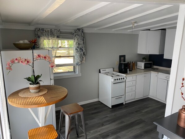 Una cocina moderna con armarios blancos, una estufa a gas, un microondas y una zona de comedor con una mesa redonda de madera y dos taburetes.