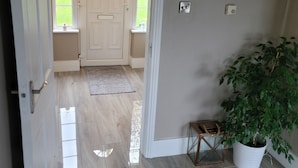 Un pasillo con suelo de madera, una puerta blanca con panel de vidrio, una pequeña planta en maceta y una lámpara de pared.