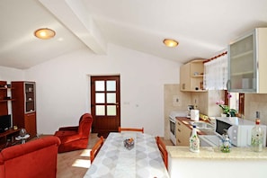 A compact living space with a dining table, red sofas, a kitchen with a microwave, and a TV. - Holiday flat with air conditioning (Baderna)