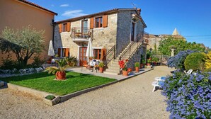 A stone building with a balcony, a staircase, and a garden with potted plants and a lawn.