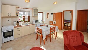 A compact kitchen with a dining area, a red chair, and a view of the outside through a window.