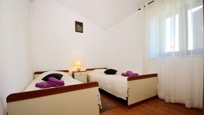 A room with two beds, a nightstand, a lamp, a small picture on the wall, and a window with curtains.