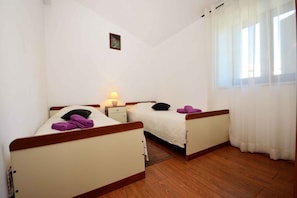 A room with two beds, a nightstand, a lamp, a small picture on the wall, and a window with curtains.