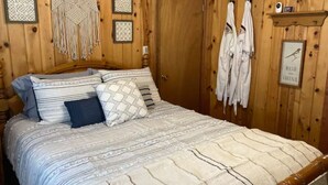 Habitación con paneles de madera, una cama, decoración de macramé en la pared y un cuadro con texto.