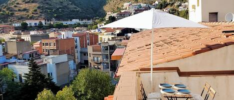 A rooftop terrace with a table set for dining, overlooking a town with buildings and hills in the background.
