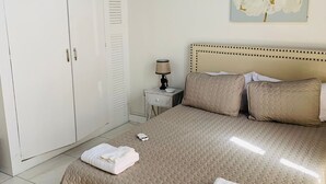 A bedroom with a large bed, a wardrobe, a bedside table with a lamp, and a wall-mounted artwork.