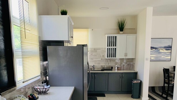 A modern kitchen with a stainless steel refrigerator, white countertops, and grey cabinets.