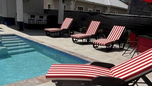 A swimming pool with red and white striped lounge chairs and a tiled deck.