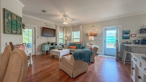 A spacious living room with a ceiling fan, a television, and a view through the glass door.