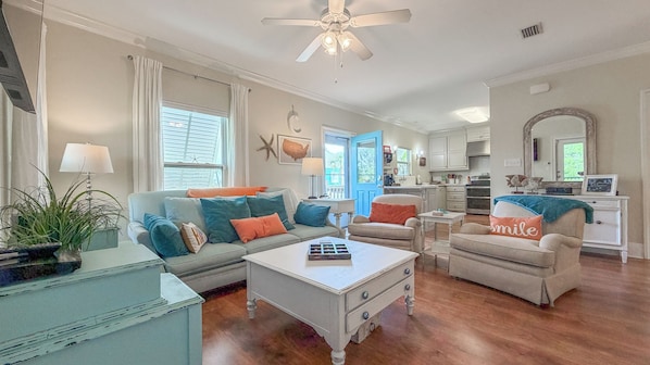 A living room with a sofa, armchairs, a coffee table, and a kitchen in the background.