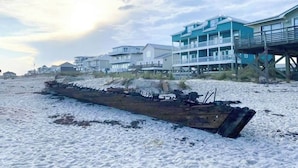 Una playa con un barco hundido y casas frente al mar.