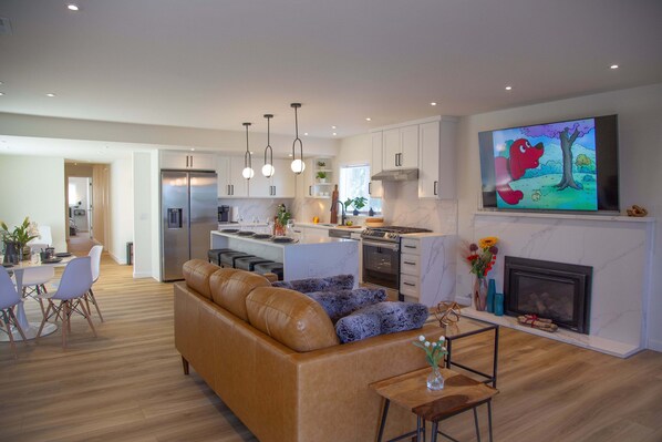 A modern kitchen with a central island, stainless steel appliances, pendant lighting, and a large flat-screen TV mounted above the fireplace. - Urban Oasis in Tacoma (Tacoma)