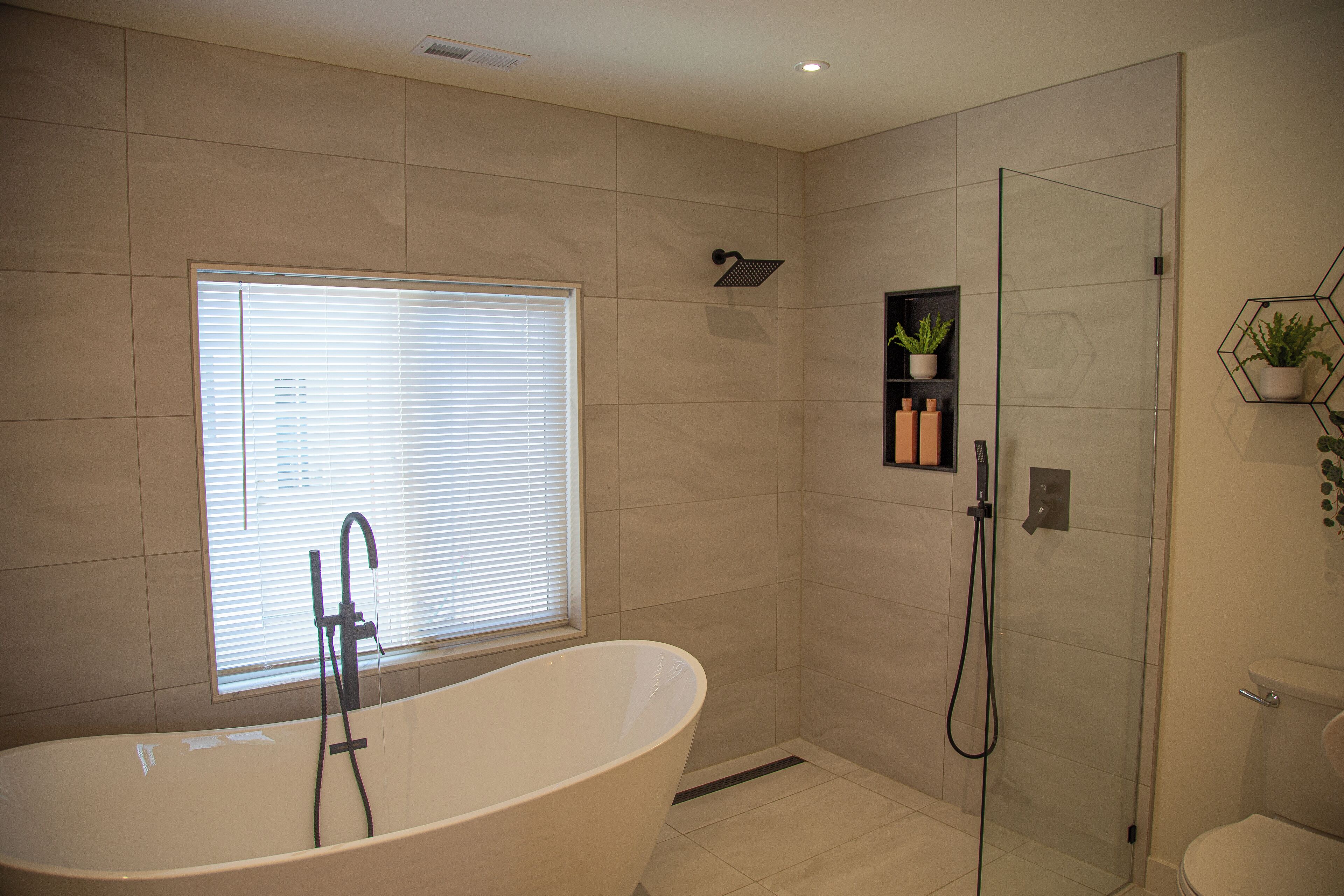 Ein modernes Badezimmer mit einer freistehenden Badewanne, einer Duschkabine aus Glas und einem Fenster mit Jalousien.