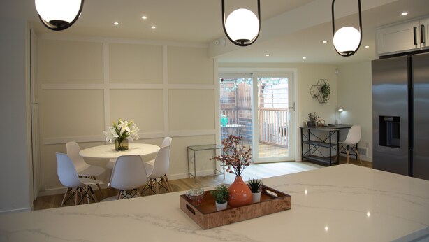 Une cuisine moderne avec un îlot en marbre, des chaises blanches et des luminaires suspendus.