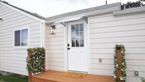 Une maison blanche avec une porte d’entrée, un porche en bois et un paillasson.