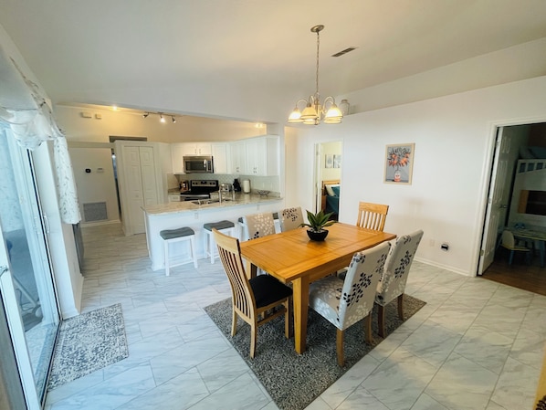 Una cocina moderna con armarios blancos, una isla central y un comedor con mesa y sillas de madera.